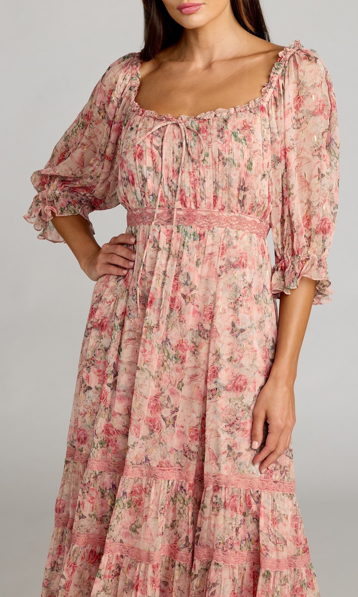 A woman poses with one hand on her hip, wearing the Mac Duggal 8330—Tea-Length Party Dress—a long, pink floral party dress featuring puffed three-quarter sleeves and a square neckline.